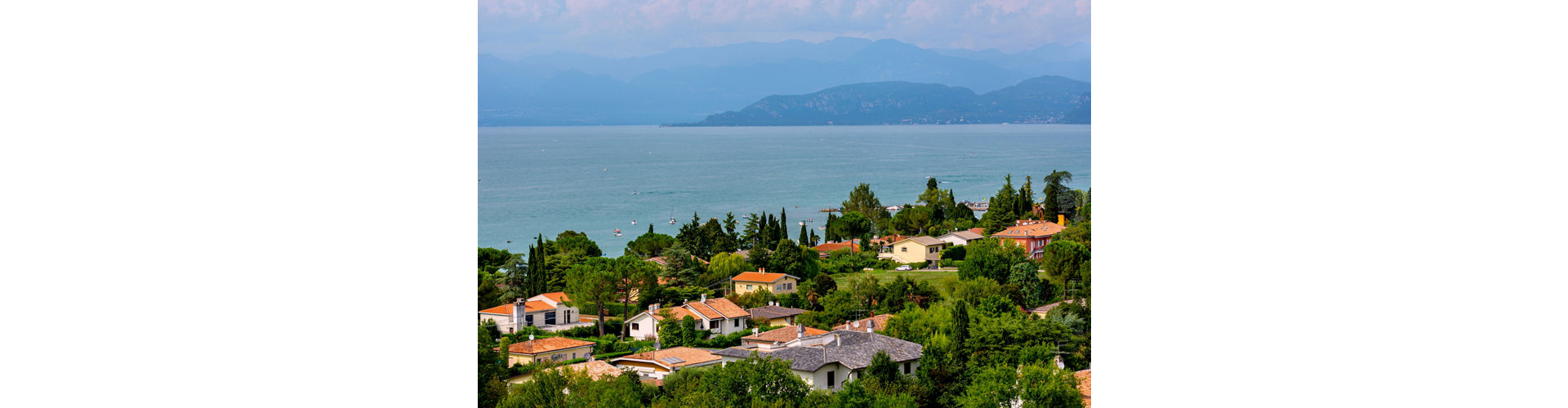 Panoramic view of Castelnuovo del Garda, featuring lush greenery, colorful houses, and boats on the serene lake waters.