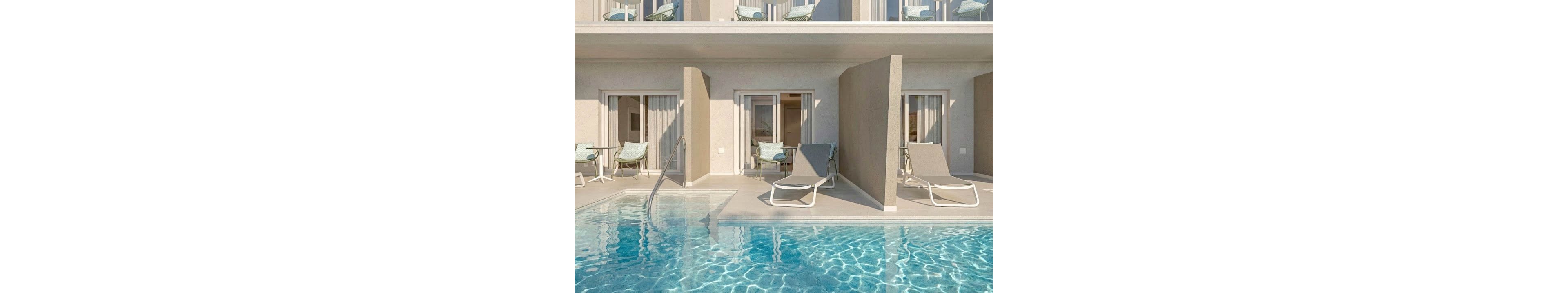 A contemporary hotel facade features ground-floor rooms opening directly onto a shared swimming pool. Each terrace has sun loungers and a small seating area behind partial privacy walls. The clear blue water reflects sunlight, creating a bright and inviting atmosphere. Upper-level balconies with chairs and tables overlook the pool area, enhancing the resort-like feel.