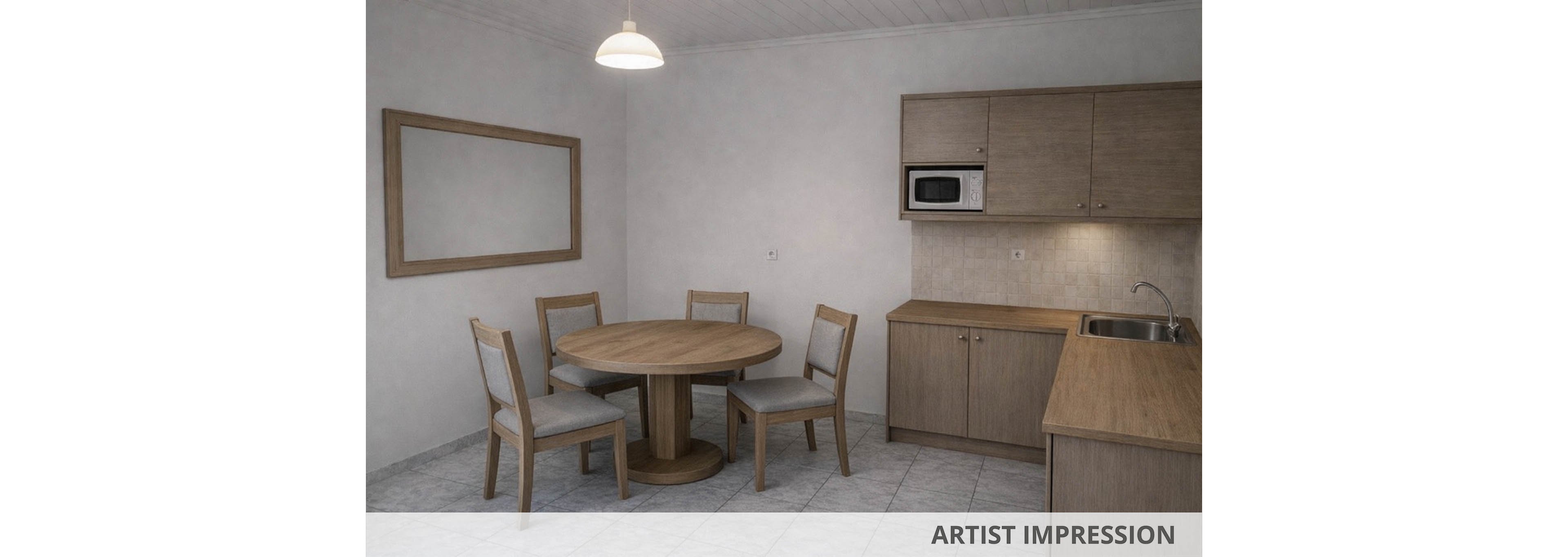 A compact kitchen features light wood cabinetry and a matching round dining table with four chairs. The space has neutral gray tiled flooring and simple off-white walls. A built-in microwave is set into the upper cabinets above a small countertop and sink. A large empty wooden frame or wall panel hangs on the left, and a single pendant light illuminates the room, creating a clean, minimalist atmosphere.