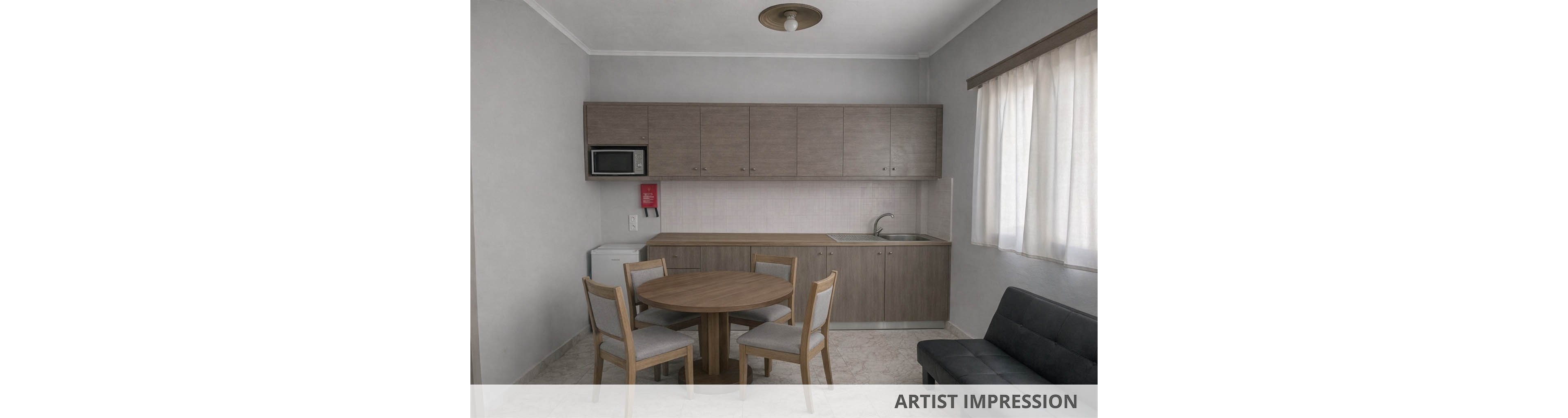 A compact studio kitchen features a round wooden dining table with four upholstered chairs in the foreground. The kitchenette includes upper and lower cabinets, a sink, a microwave, and a small refrigerator against a light-colored wall. A black sofa sits to the right near a large window with sheer curtains, allowing soft daylight into the room. The neutral color palette and simple furnishings create a clean, minimalist atmosphere suitable for a small apartment or vacation rental.