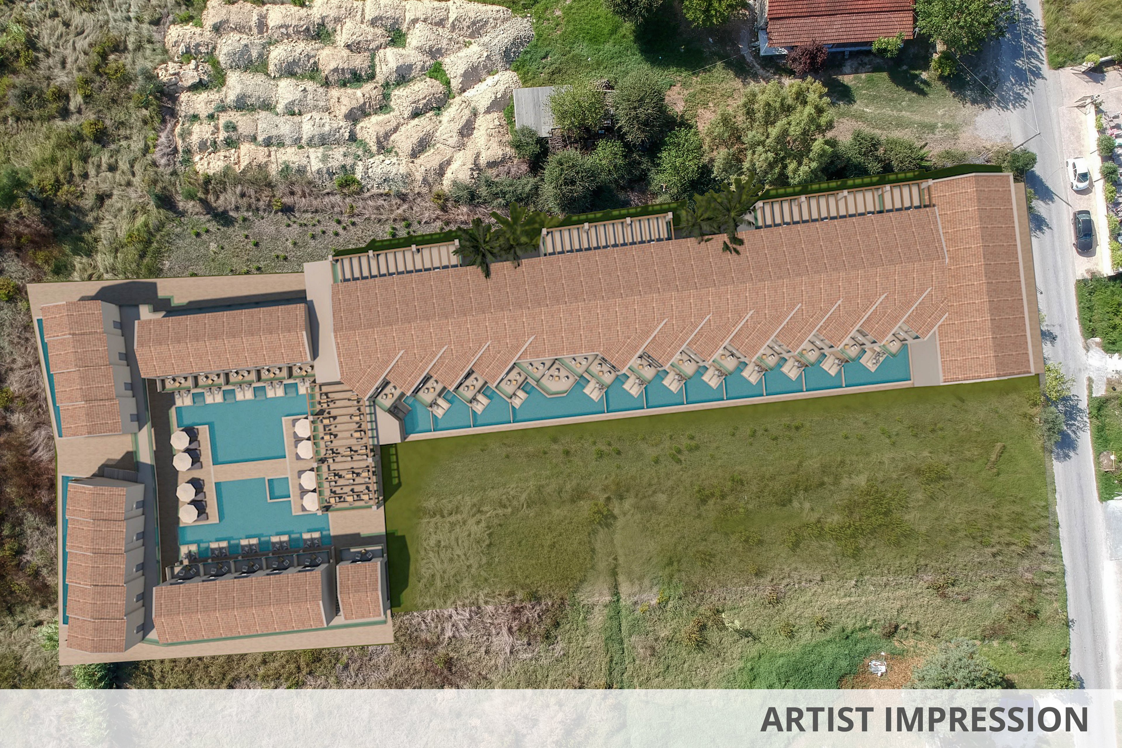 This aerial photograph captures a modern resort complex with a central swimming pool and sun loungers arranged in a geometric pattern. The building features a terracotta roof and is surrounded by green open land and nearby rural structures. The setting suggests a tranquil, vacation-oriented atmosphere with clear separation between the resort and natural landscape. No visible text or numbers are present in the image.